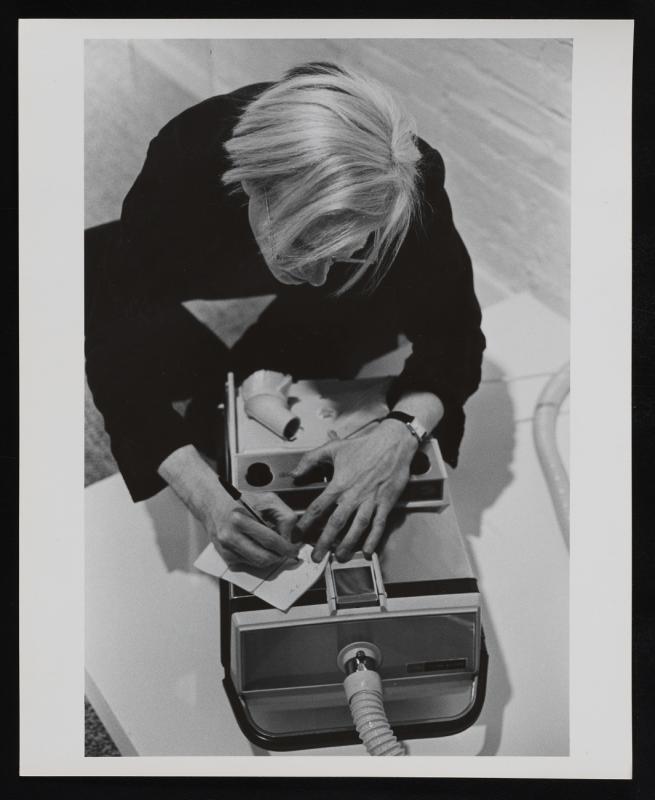 Karen Maynor, Photograph of Andy Warhol writing a note on vacuum cleaner at “Art in Process V” exhibition, 1972. 