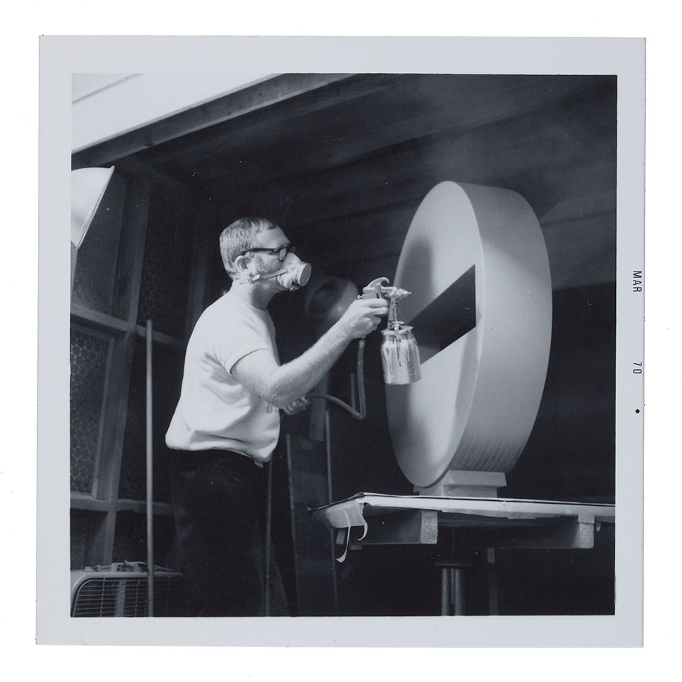 Tony DeLap in his studio spray painting a sculpture