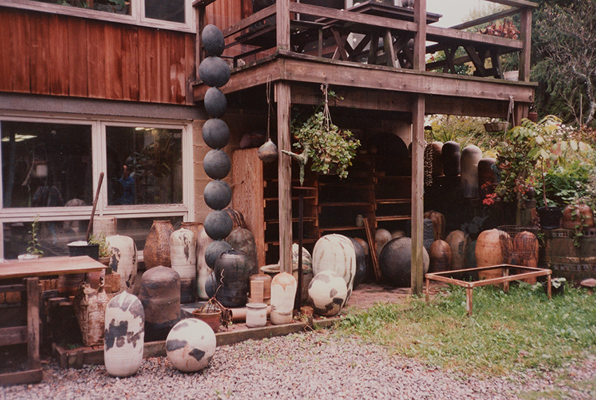 Exterior of studio with hanging plants and large collection of ceramic pots.