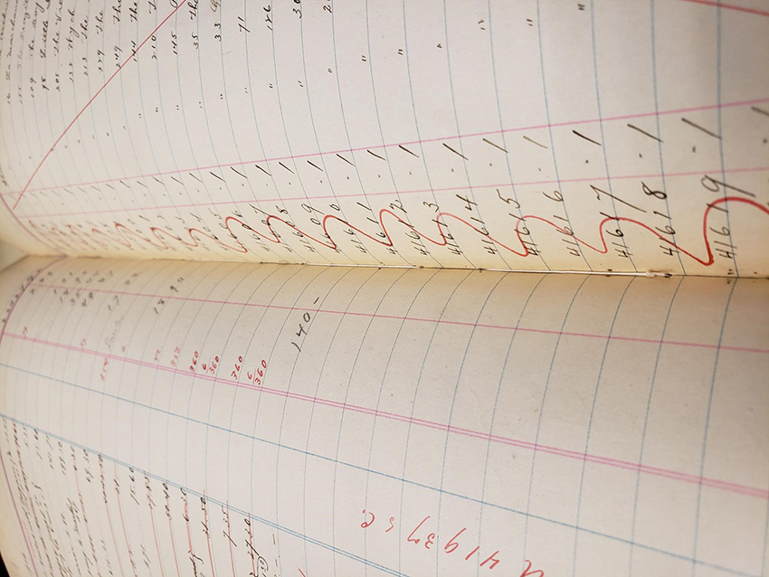Close up interior view of volume with writing in red and black ink on lined pages and and thread showing from the newly sewn binding
