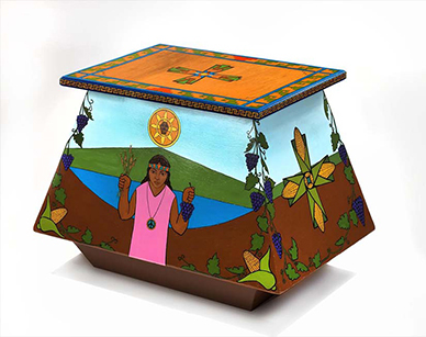 Wooden altar painted in bright colors where a crucifix with a brown-skinned Christ is on one side; on the other, an indigenous woman in pink holds wheat stalks and grapes. Corn and grape vines are decorative elements to the altar. 