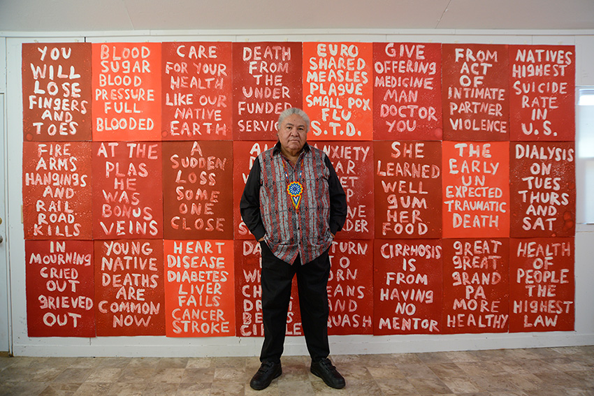 Man standing against a wall full of red canvases with white text
