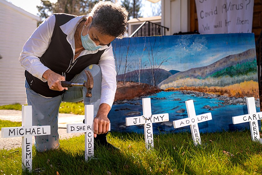 A woman outside of a church crouched on the ground hammering white wooden crosses, with names written in black, into the ground.