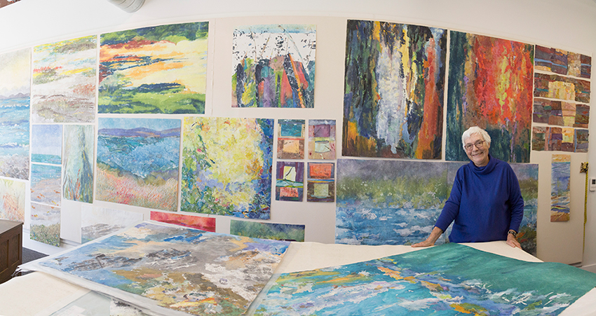 Woman with white hair wearing a blue sweater and glasses in her art studio.