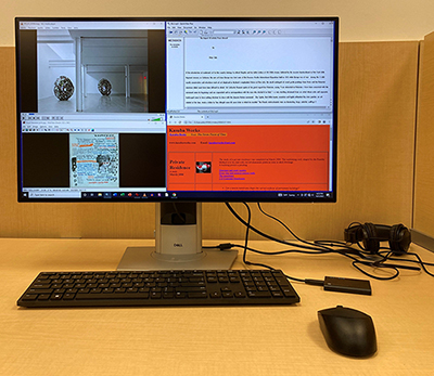 ALT Computer set in a wood cubical with black keyboard, mouse, external drive, and headphones. The screen shows various programs for accessing born-digital material. 