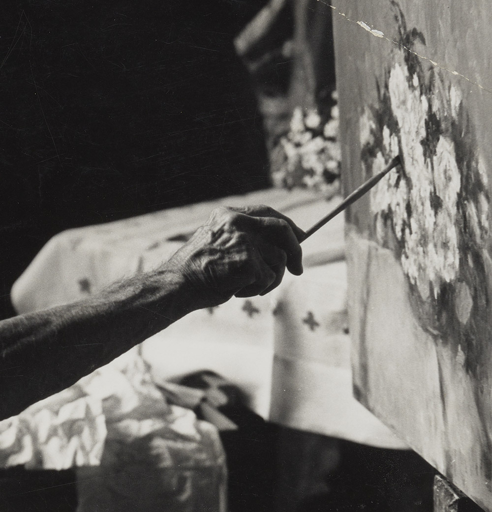 Detail of grayscale photograph of F. Edwin Church extending his right arm and brush to paint a still life of a flower arrangement.