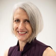 Close-up photograph of Anne Helmreich, smiling with chin-length hair and wearing a dark blouse.